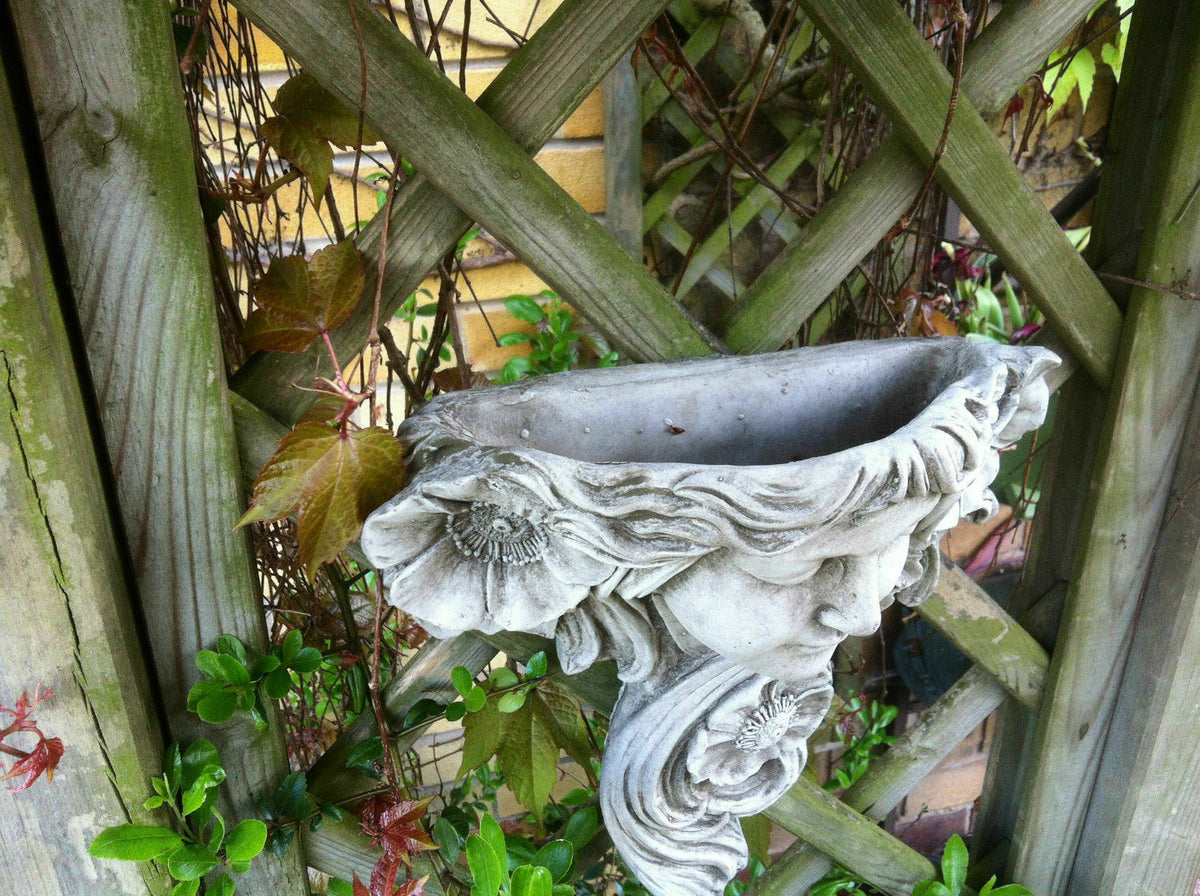 Side view of Art Nouveau Lady Wall Decor showing planter-style depth, mounted on a wooden trellis with climbing plants in a garden.