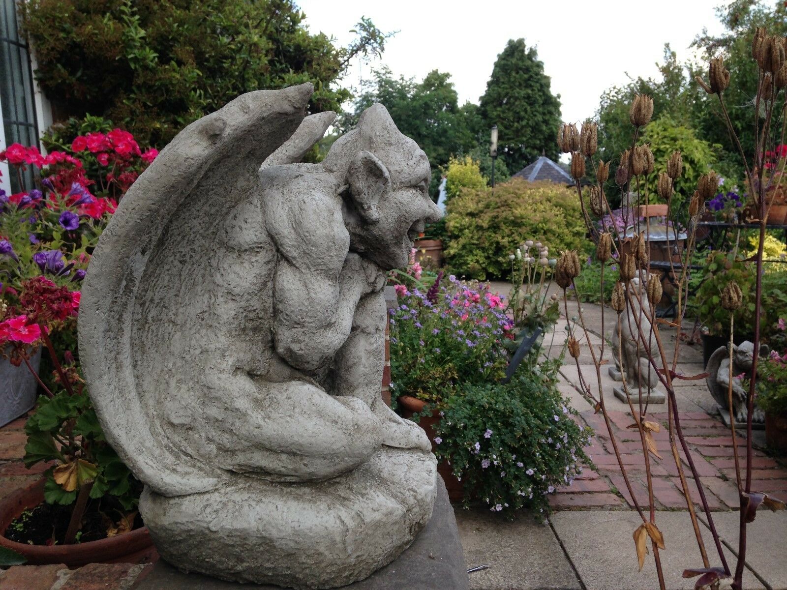 Side view of Winged Gargoyle Garden Ornament showing detailed stone texture and muscular wings, set in a vibrant garden patio setting.