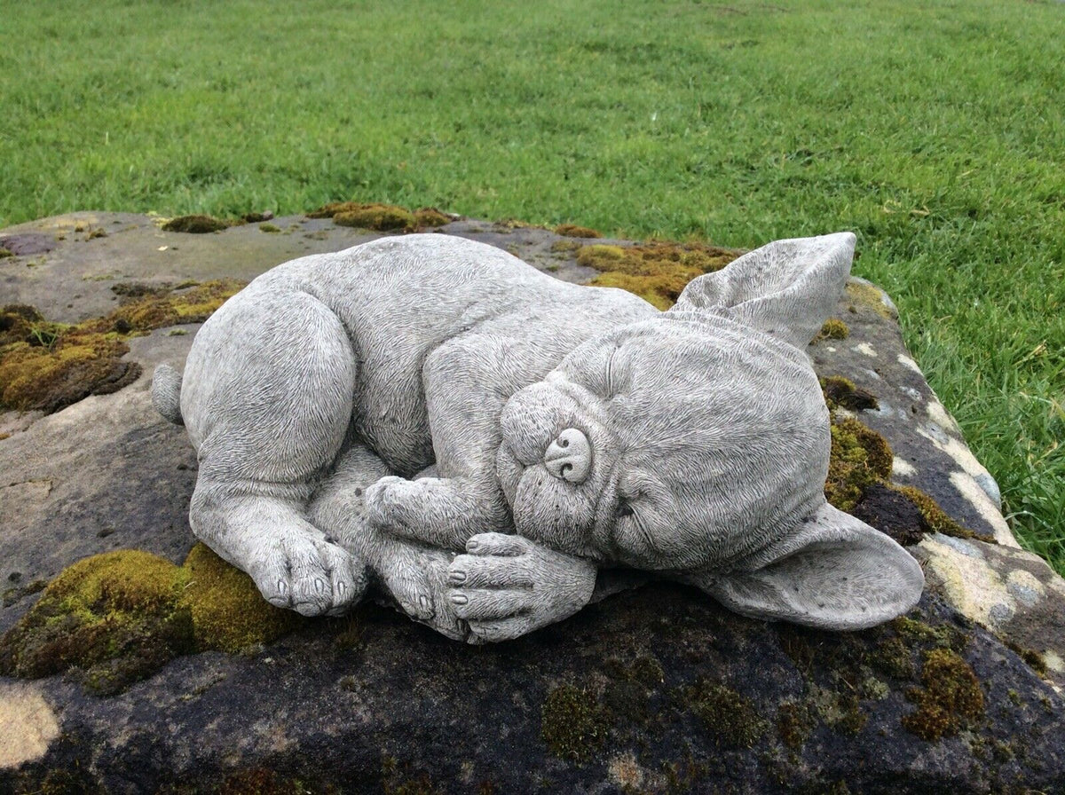 Realistic stone French Bulldog garden ornament curled up on moss-covered rock, a charming addition to home and garden decor.