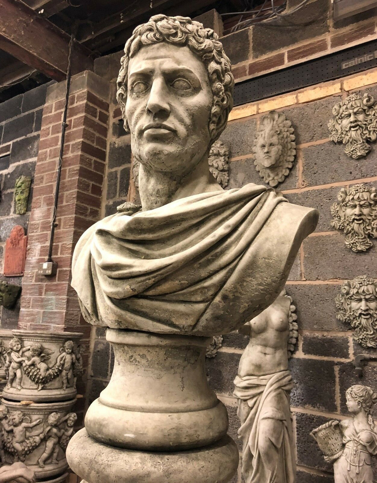 Upward angle of Stone Marc Anthony Bust Statue on limestone pedestal, emphasizing Roman craftsmanship for decorative outdoor use.