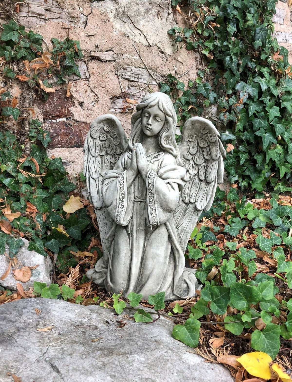 Elegant Stone Praying Angel Statue nestled among ivy and leaves, perfect as a spiritual garden ornament or lawn sculpture.