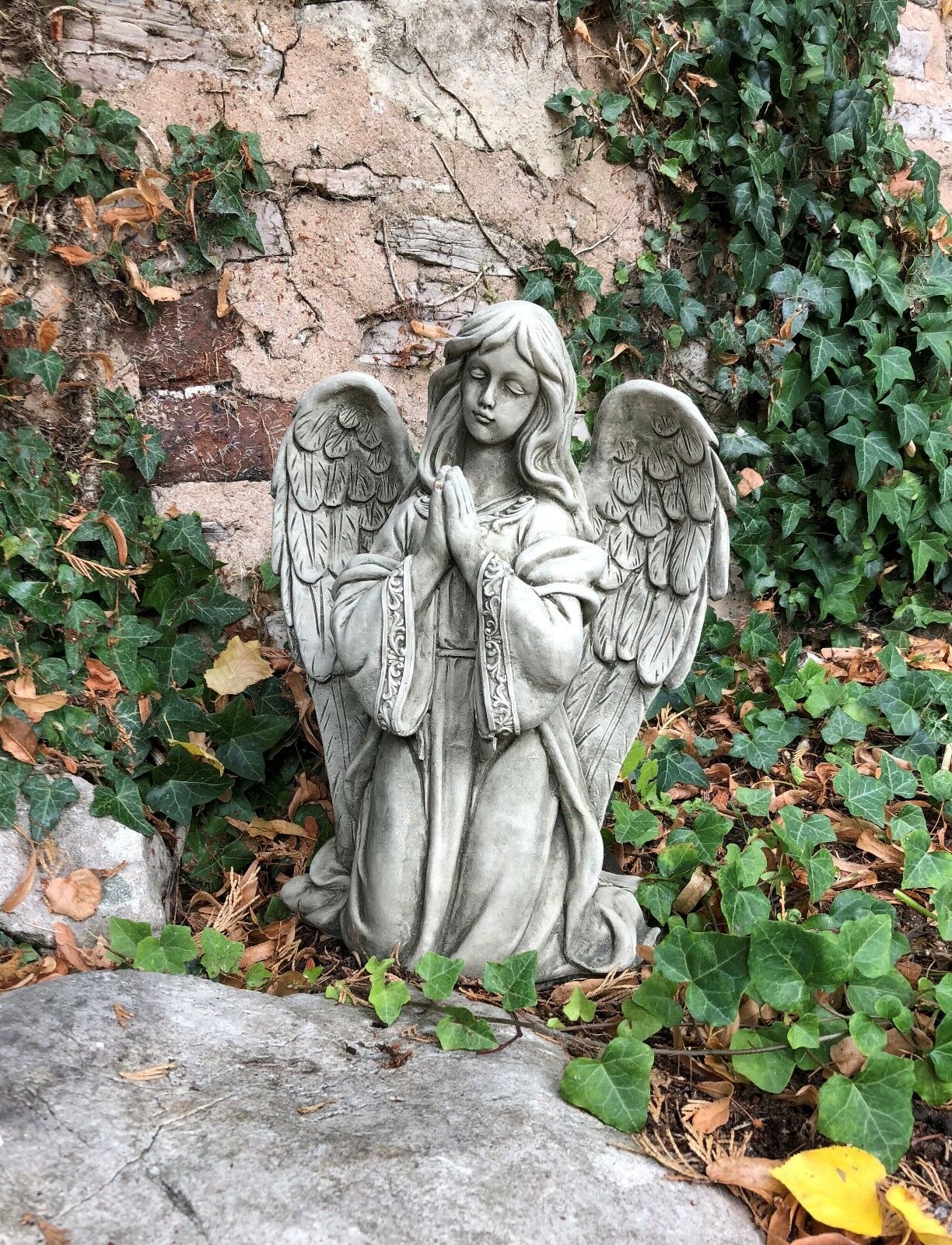 Elegant Stone Praying Angel Statue nestled among ivy and leaves, perfect as a spiritual garden ornament or lawn sculpture.