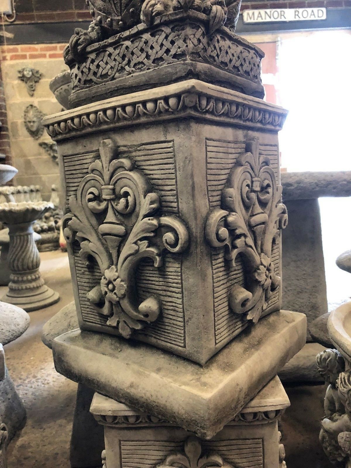 Intricate garden plinth in square stone design featuring carved floral details. Solid and heavy for supporting statues in outdoor settings.