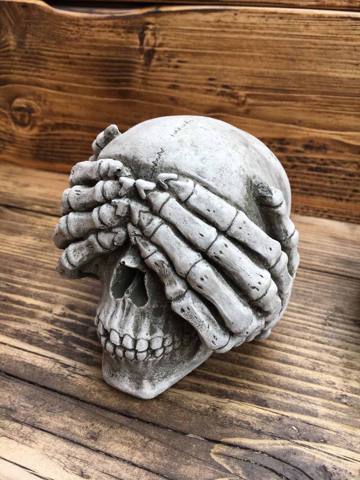 Close-up of 'See No Evil' skull garden ornament made from solid limestone, showcasing skeletal hands covering the eyes with detailed antique texture.