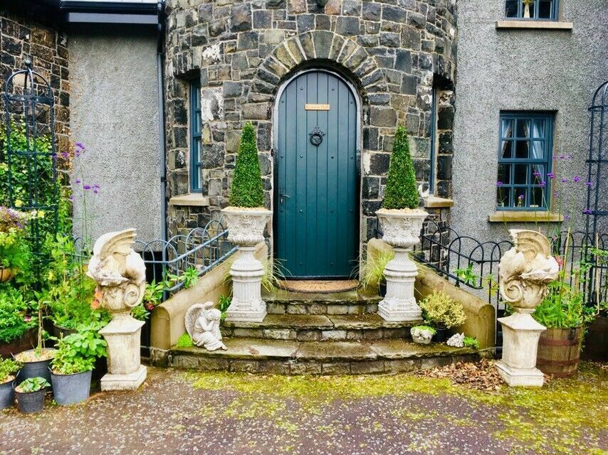 Pair of stone Bacchus design urn planters on plinths flanking a castle-style entrance, enhancing the garden's classical elegance.