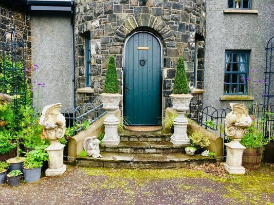 Pair of stone Bacchus design urn planters on plinths flanking a castle-style entrance, enhancing the garden's classical elegance.