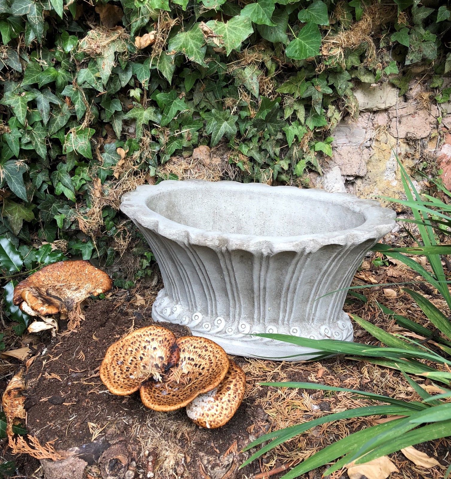 Durable fluted garden pot planter in stone finish, set against ivy-covered wall, perfect for stylish outdoor planting.