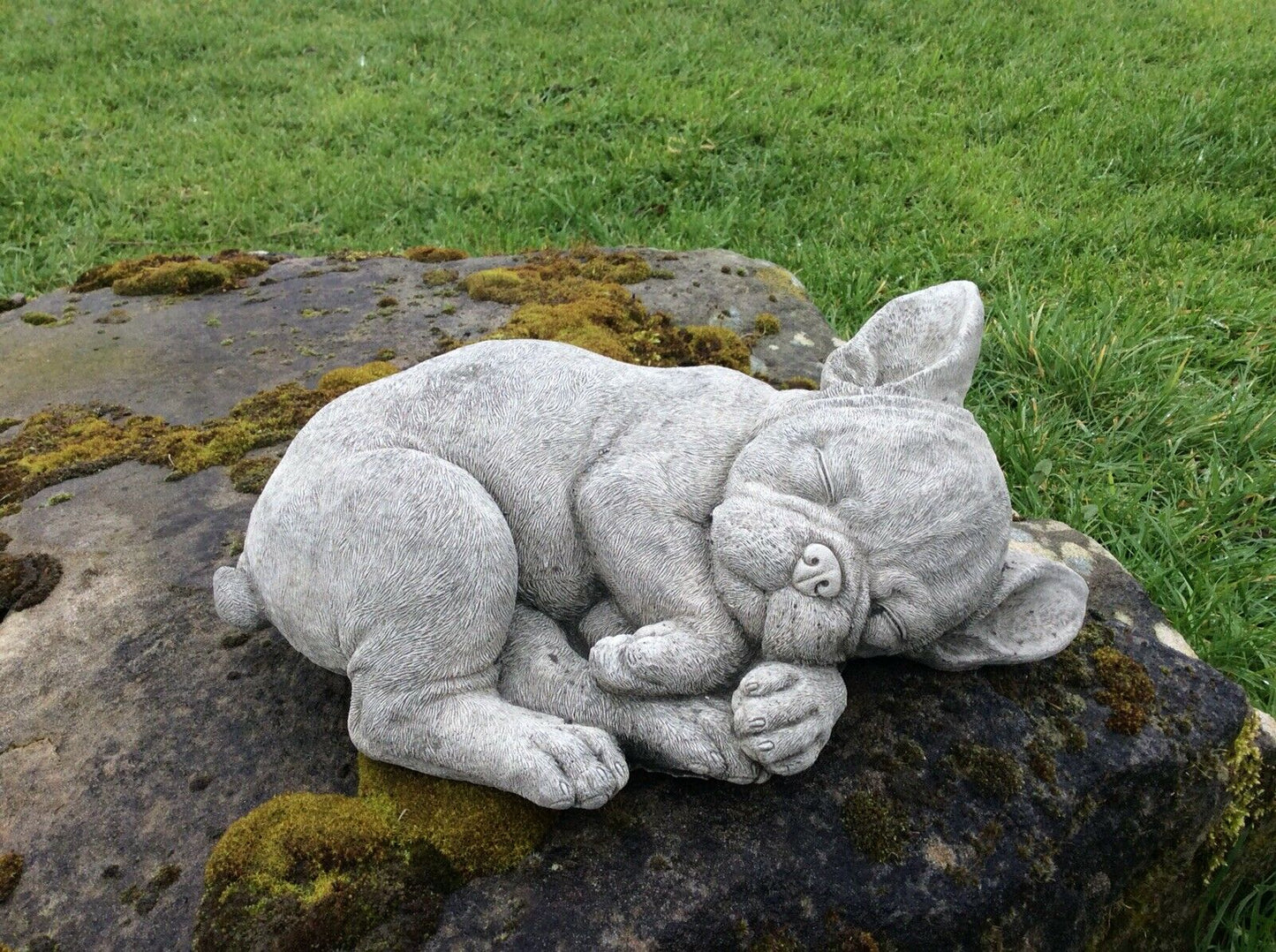 Handmade stone French Bulldog sleeping statue on rock, durable and weather-resistant for garden or lawn ornamentation.