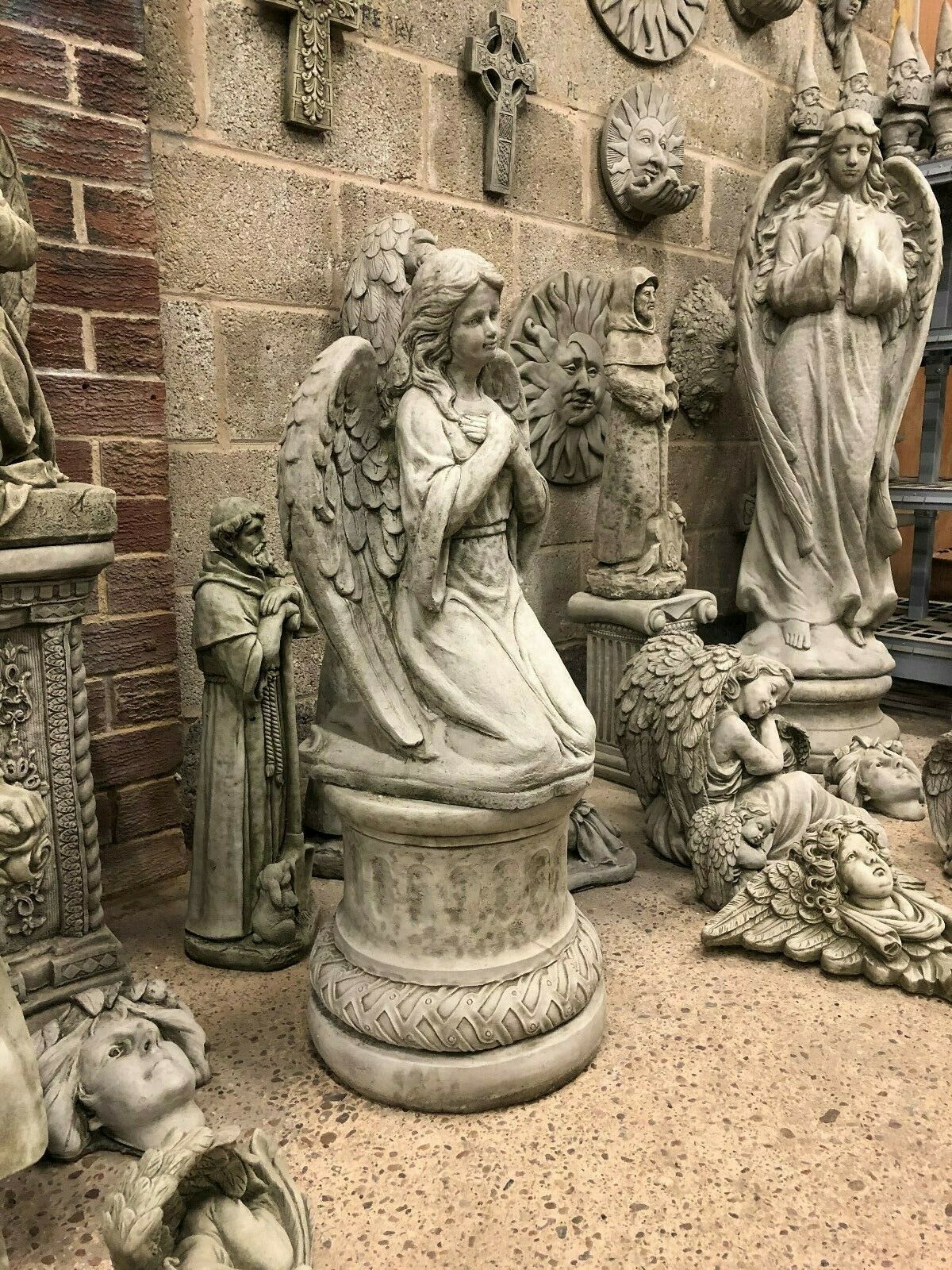 Antique limestone angel statue displayed among other garden sculptures, ideal for religious or memorial-themed garden settings.