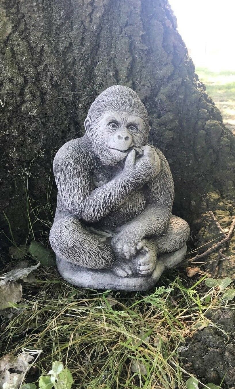 Stone gorilla garden statue in antique grey sitting at tree base, a charming animal ornament for outdoor home and garden decoration.