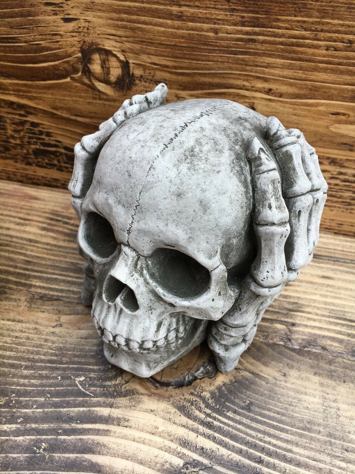 Side view of 'Hear No Evil' skull garden ornament with skeletal hands over ears, made from weather-resistant limestone for patio or lawn decoration.