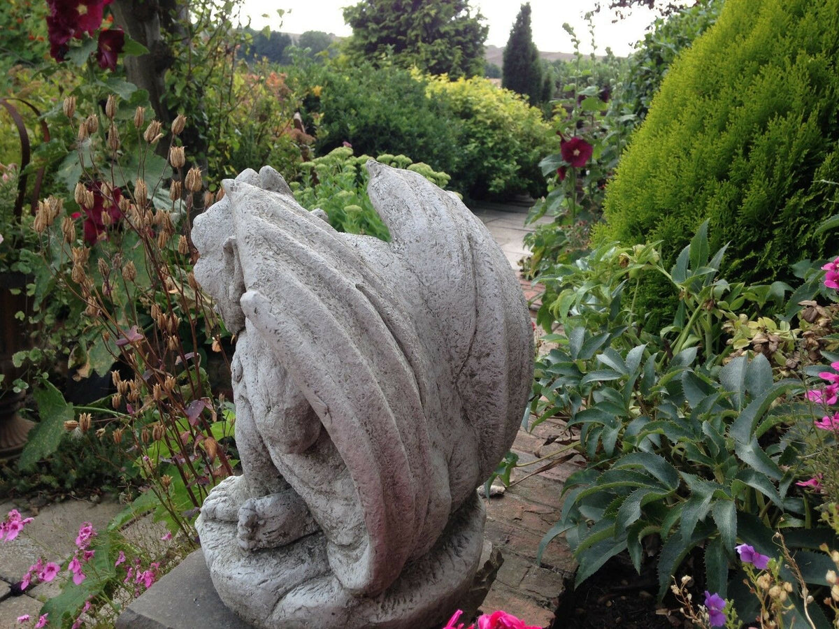 Rear view of Winged Gargoyle Garden Ornament showing curved wings and textured stone design, nestled among lush garden plants and flowers.