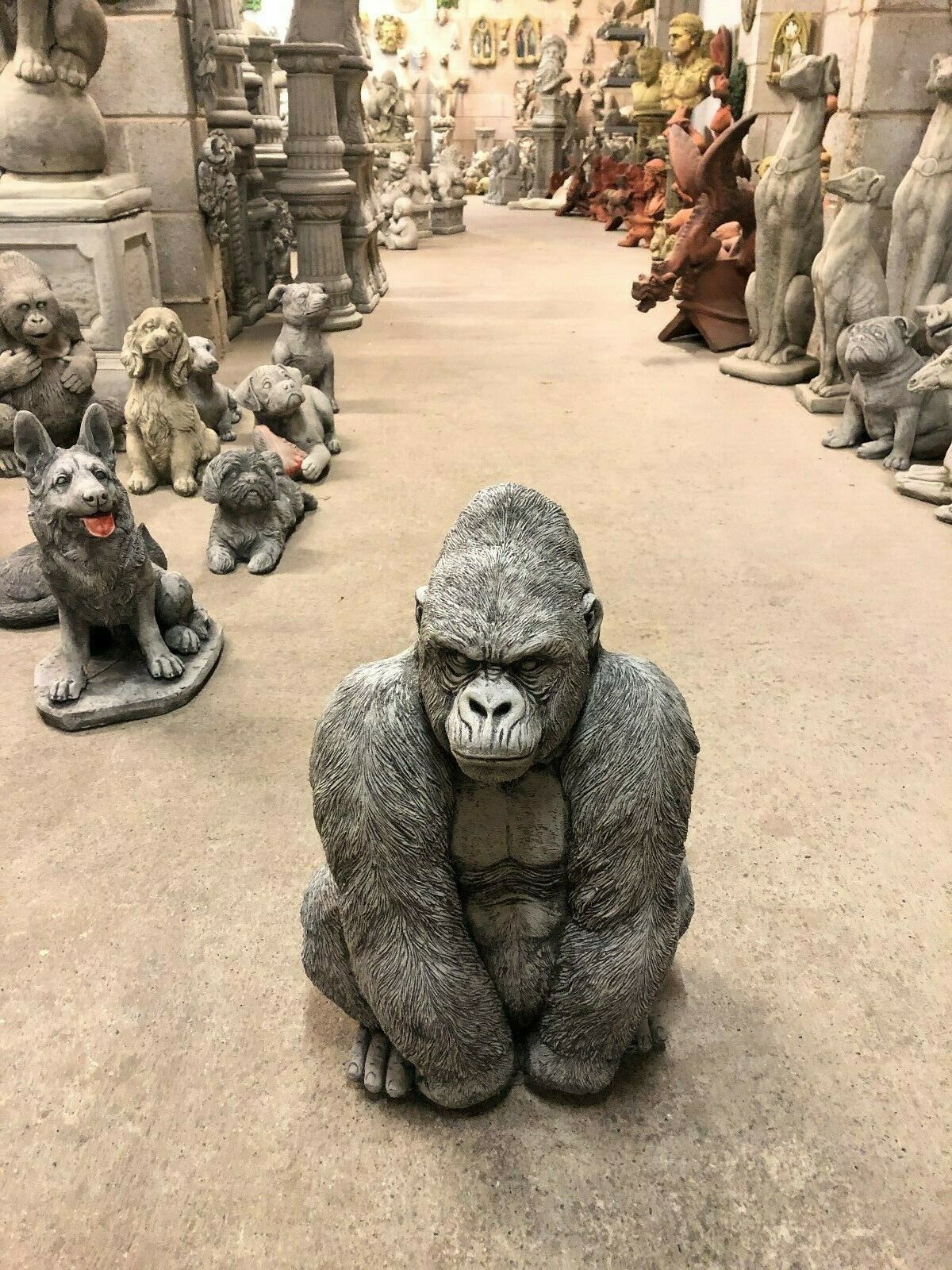 Stone Silverback Gorilla Statue centered in a sculpture showroom, surrounded by other animal ornaments for home and garden decor.