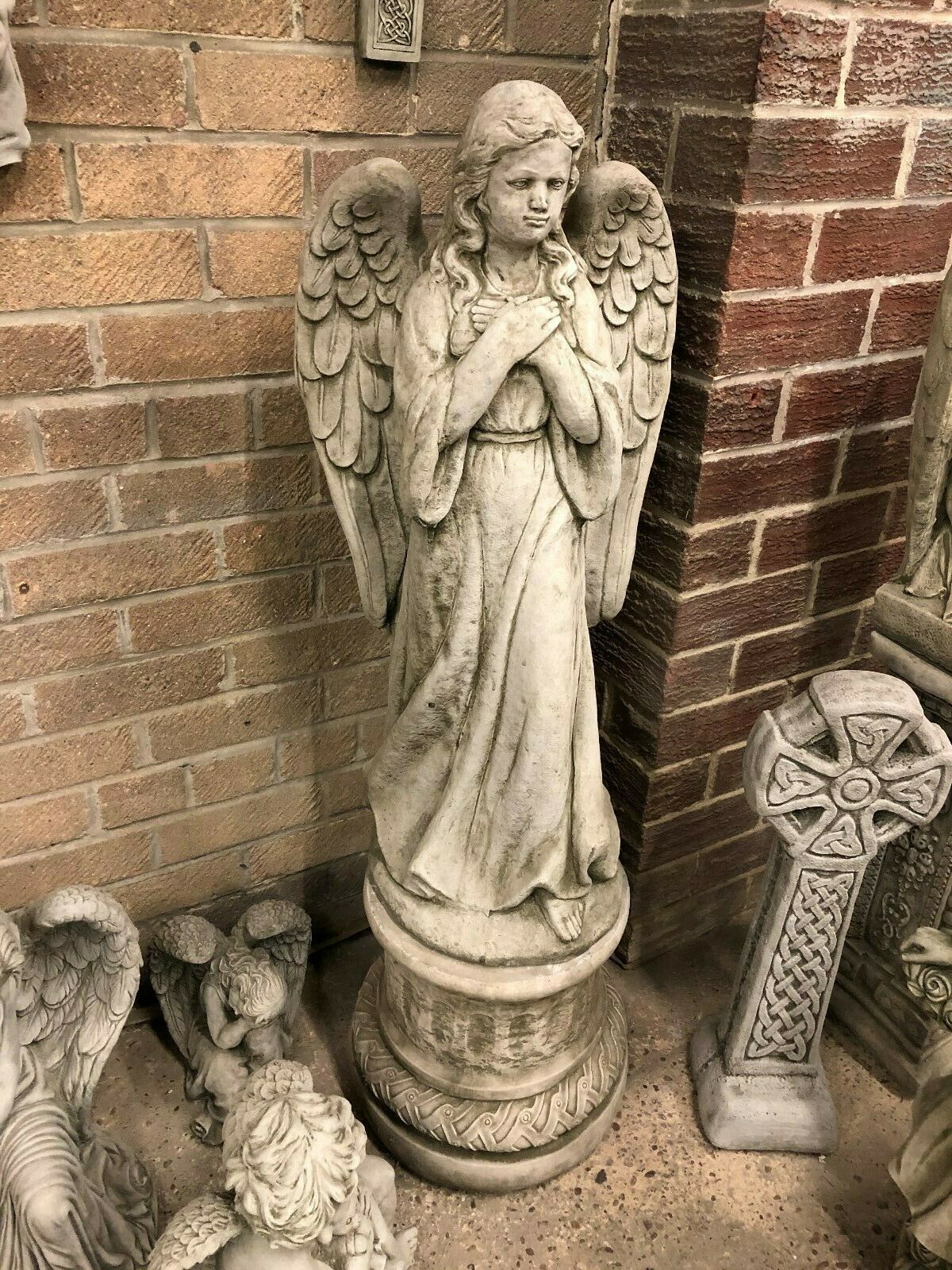 Weather-resistant stone angel pedestal statue featuring detailed wings and antique finish, perfect for garden or patio ornamentation.