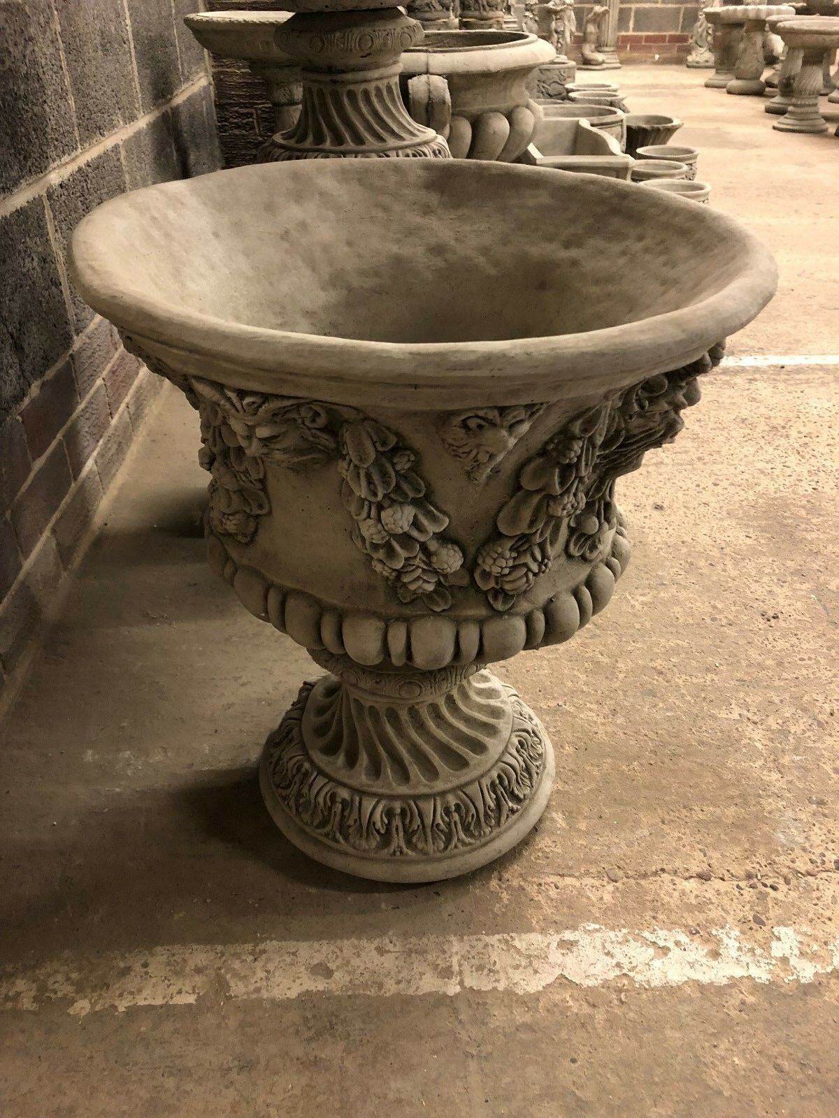 Angled view of a Bacchus design stone urn planter with wide bowl and ornate base, suitable for outdoor plant arrangements.