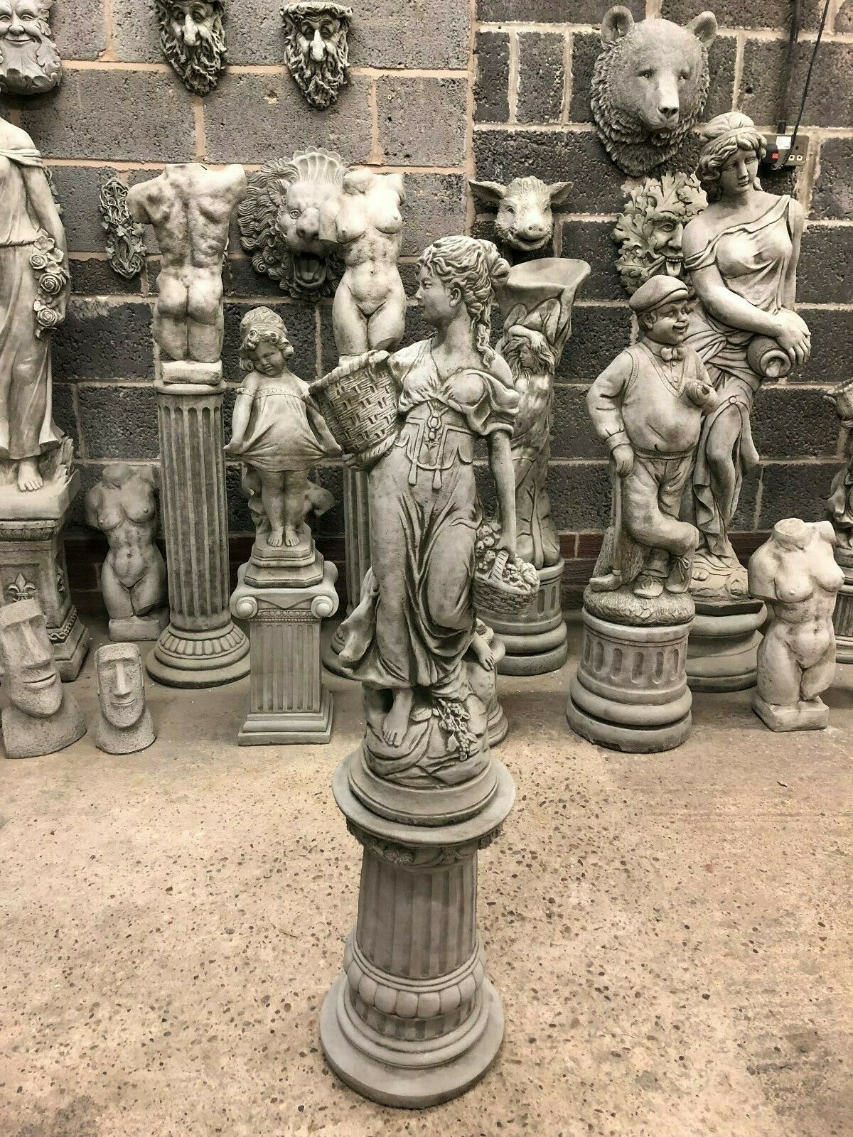 Stone Roman Lady Garden Statue in limestone on fluted plinth, surrounded by classical sculptures, ideal for outdoor antique-style decor.