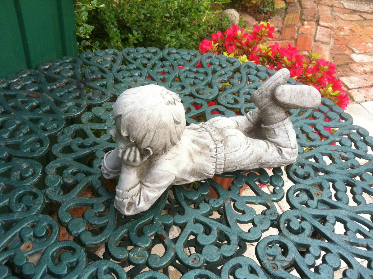 Close-up of stone garden ornament boy figure laying on ornate metal table. Durable limestone sculpture with antique finish for outdoor decor.