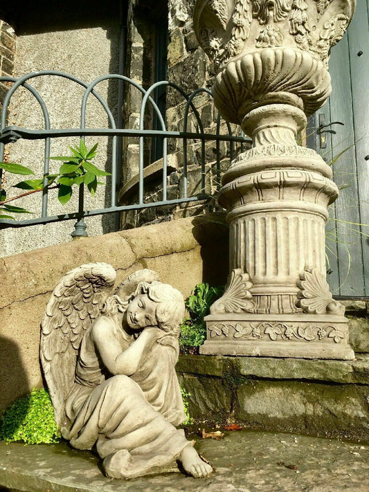 Garden Angel Statue - Large Stone Winged figure resting beside a classical urn on stone steps, ideal for antique-style garden decor.