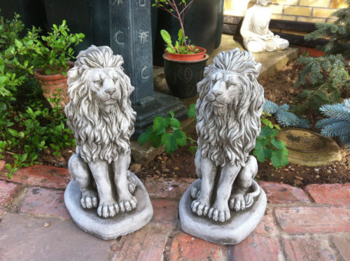 Two matching stone lion statues sitting on a garden path, enhancing outdoor decor with a regal and durable design.