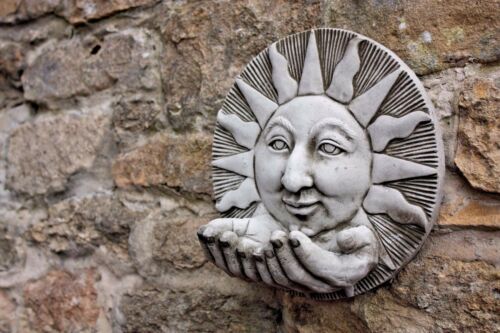 Garden Bird Feeder - Stone Sun Design mounted on rustic stone wall. Features smiling sun face with outstretched hands for bird food placement.