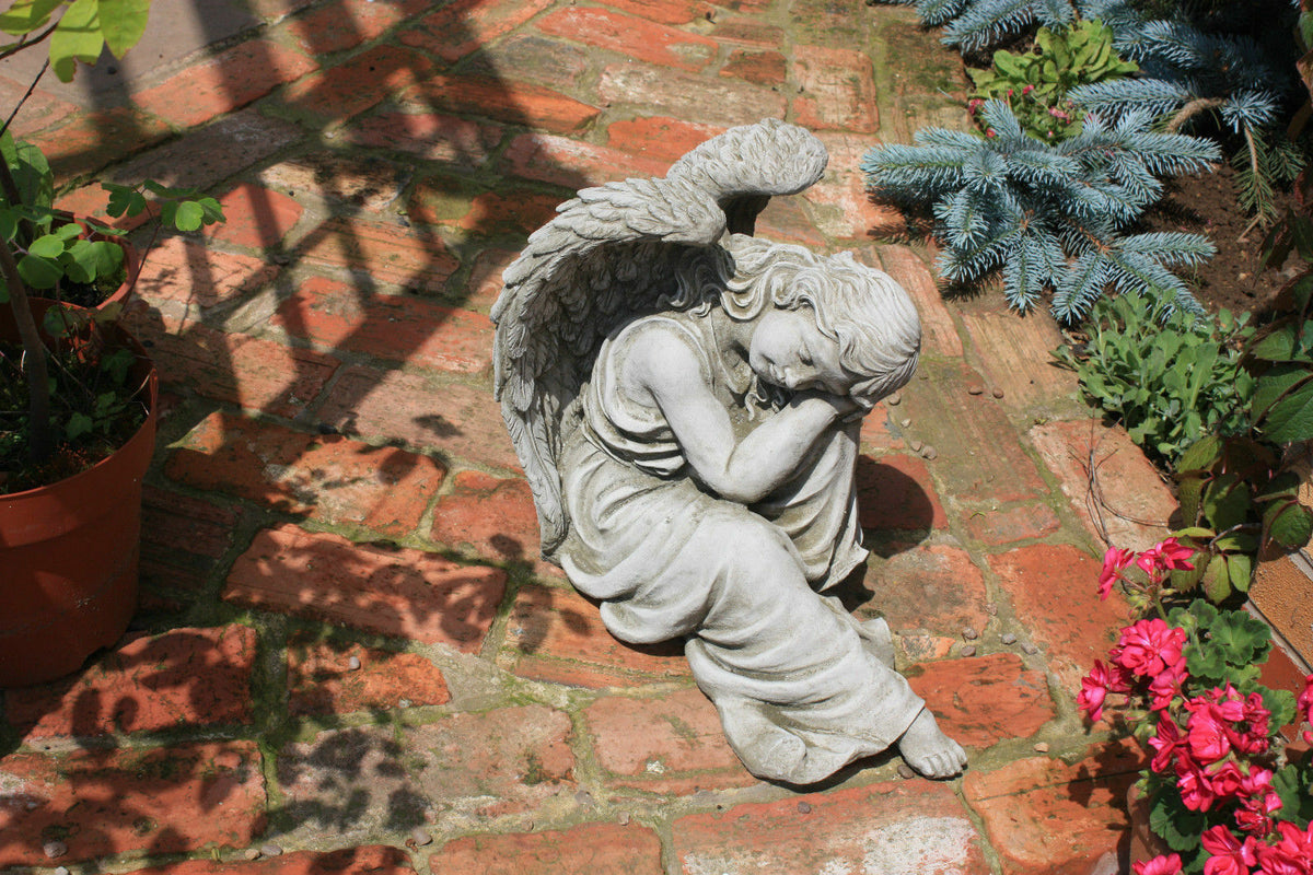 Large Stone Winged Angel Statue placed on red brick patio surrounded by flowers, perfect for enhancing garden ambiance with spiritual charm.
