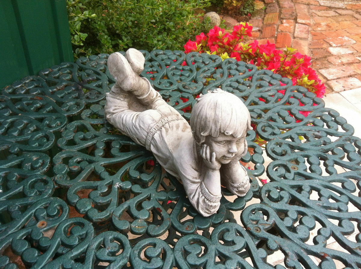 Front view of stone garden ornament boy laying with hands on cheeks. Antique finish adds charm to garden or patio spaces.