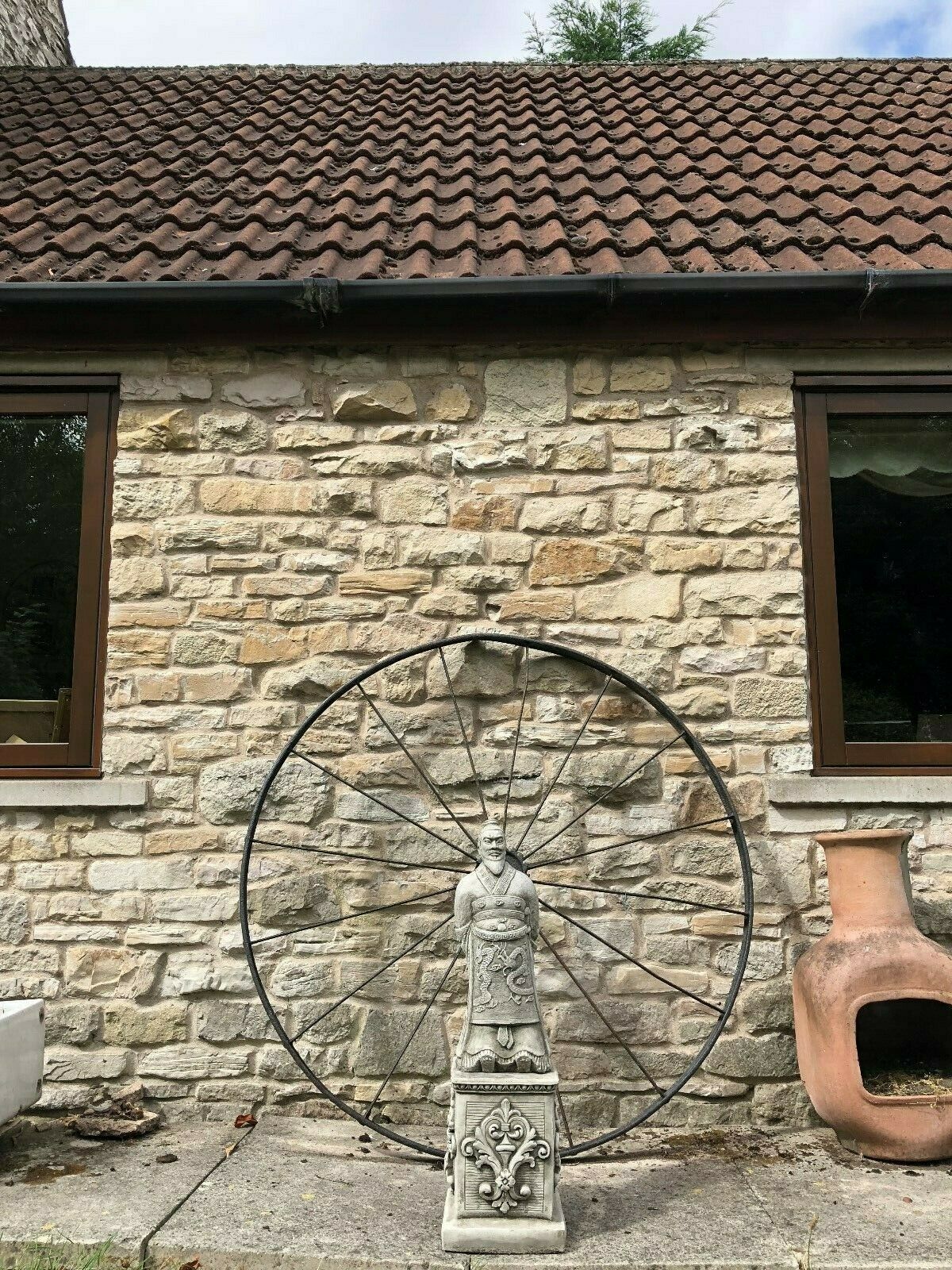 Full outdoor scene featuring the Zhan Shi Warrior Garden Statue in front of a stone house wall, ideal for patio or lawn ornamentation.