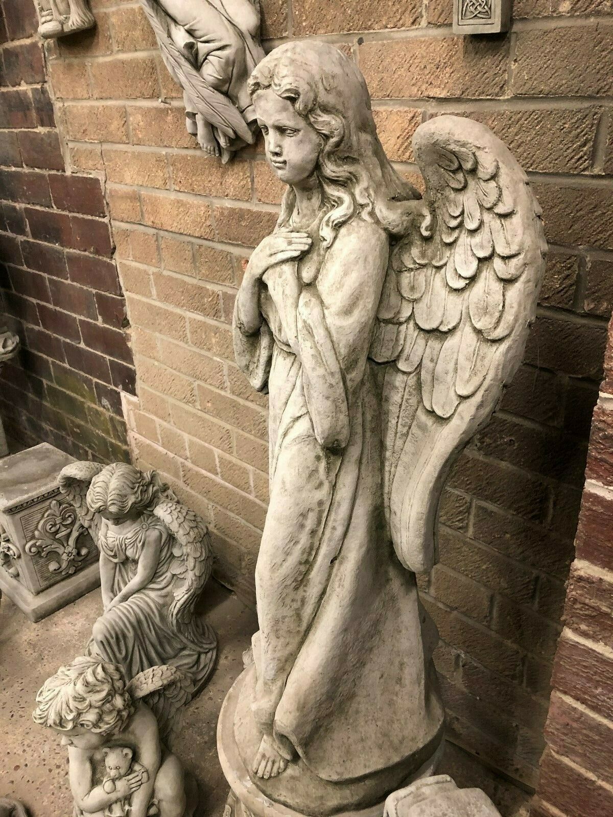 Side view of stone angel pedestal statue with intricate wing and robe detailing, designed for garden or lawn decoration.