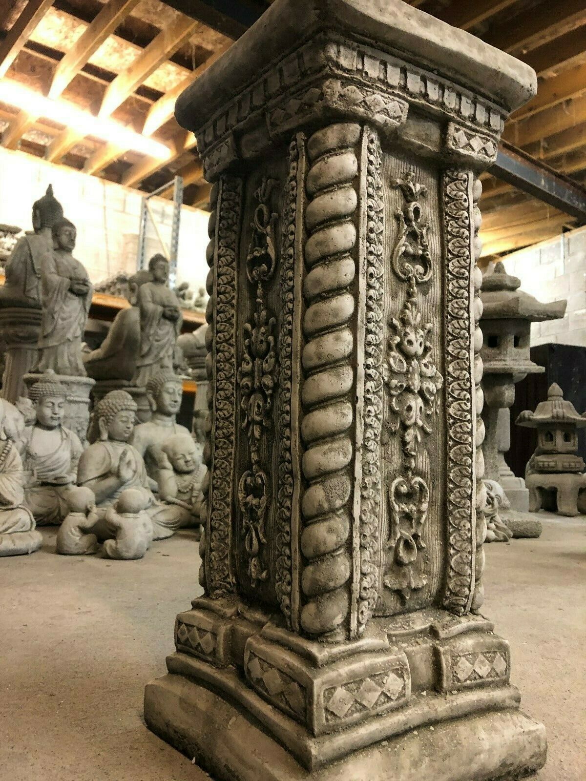 Close-up of tall stone garden column with heavy antique finish, highlighting detailed floral and rope carvings on limestone surface.