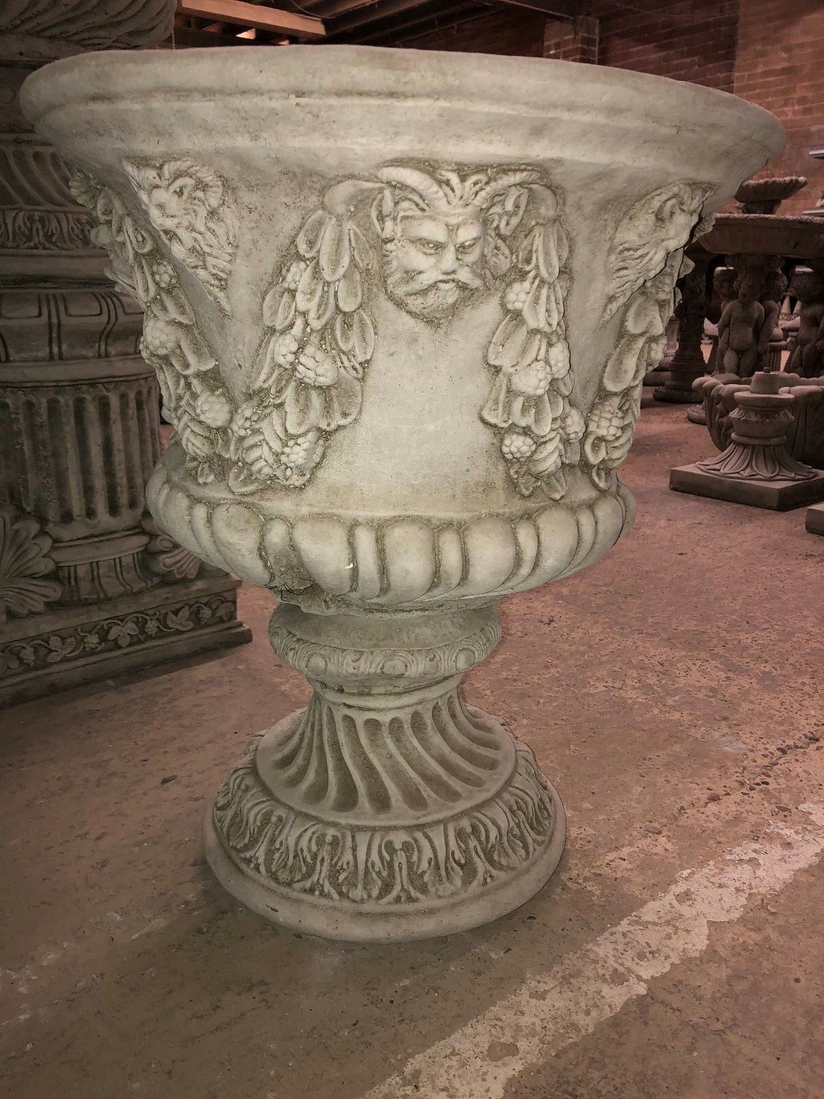 Close-up of Bacchus face and garland details on a stone urn planter, emphasizing its decorative and historical garden appeal.
