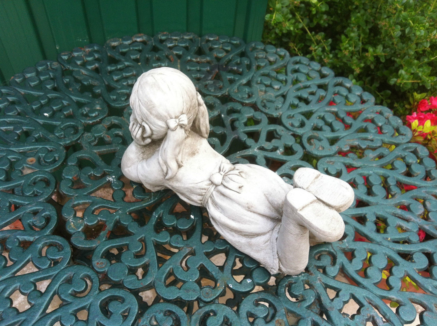 Rear view of stone garden ornament girl laying with pigtails and dress. Weather-resistant limestone ideal for garden decoration.