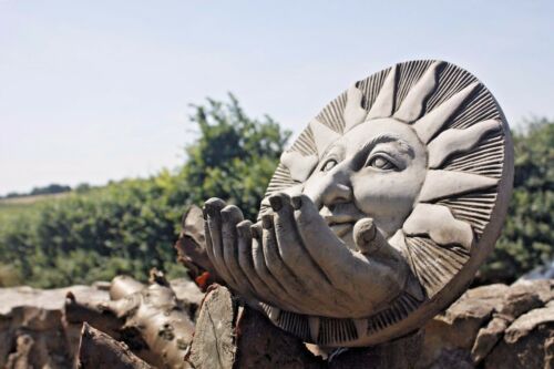 Durable Limestone Garden Bird Feeder with sculpted sun face and hands, positioned outdoors with scenic countryside background.