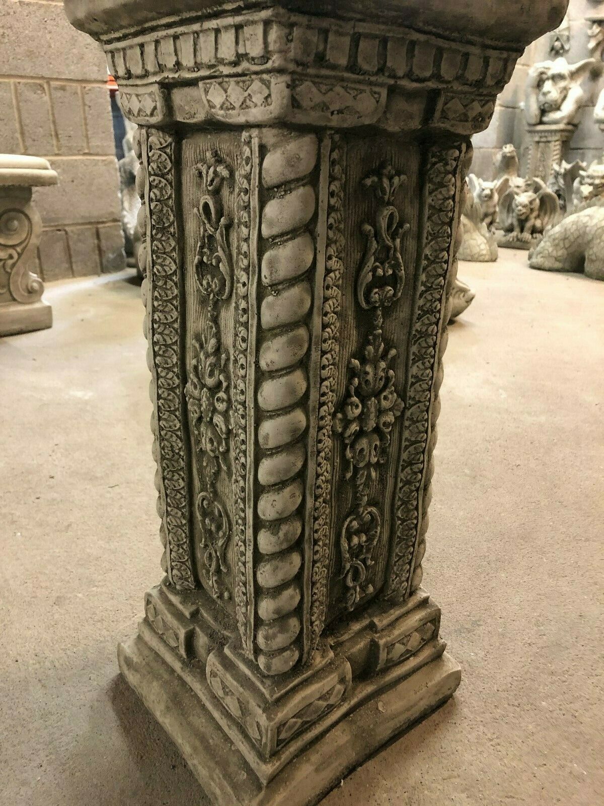 Decorative stone garden plinth with ornate vertical patterns and robust base, designed for outdoor sculpture or planter display.
