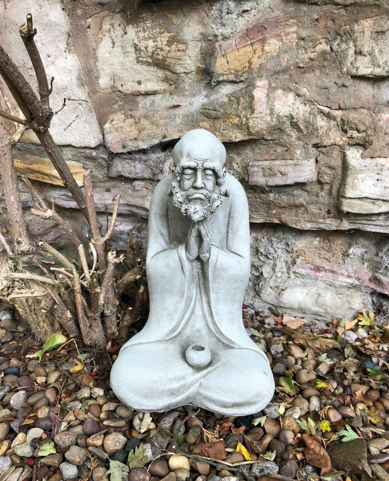Front view of the Stunning Stone Praying Old Monk Sculpture Garden Ornament placed on pebbled ground, enhancing outdoor serenity.