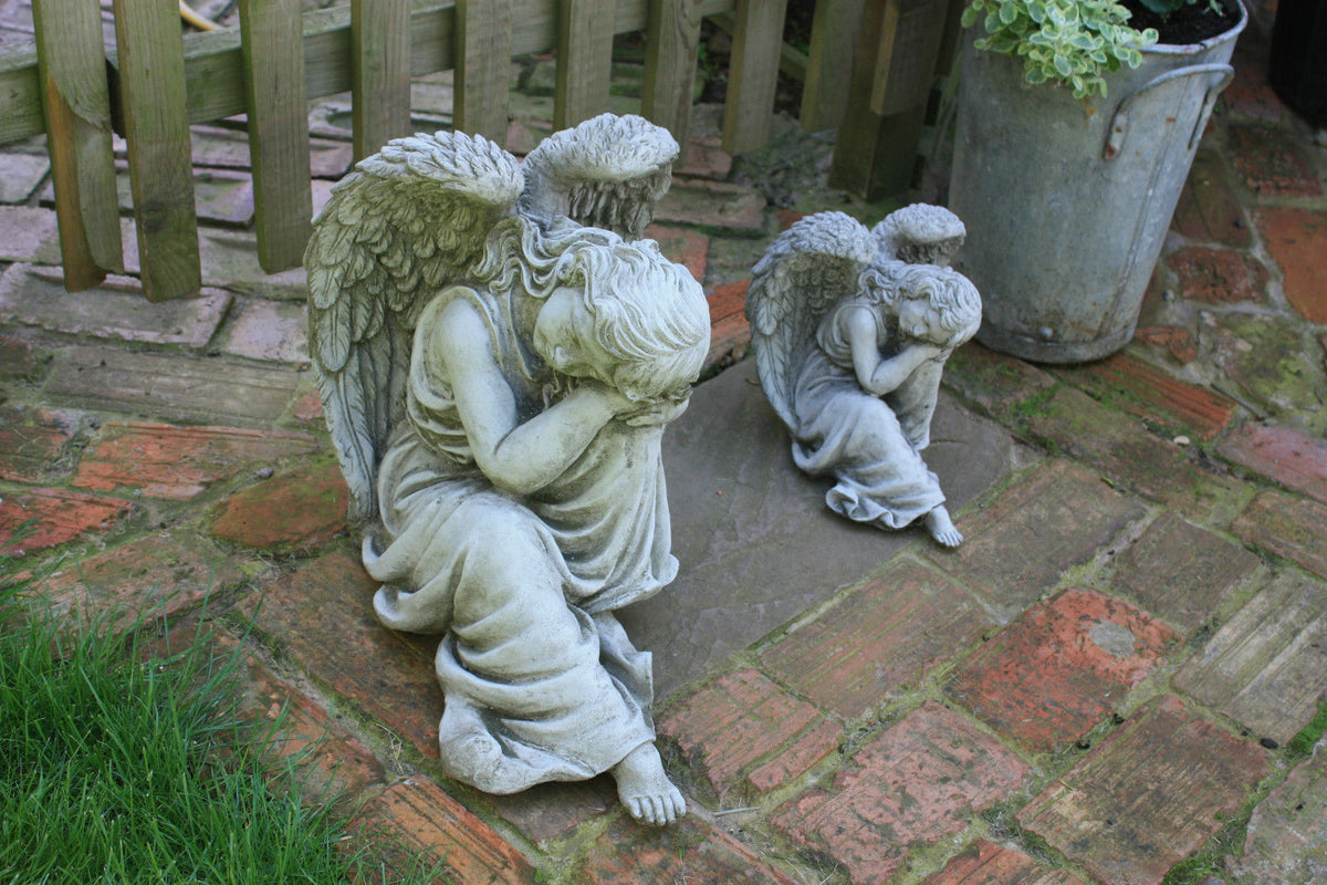 Two Large Stone Winged Angel Statues in seated pose on brick path, ideal as matching garden ornaments for tranquil outdoor spaces.