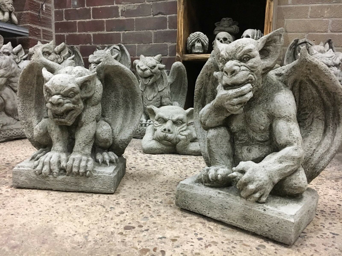 Pair of stone gargoyles with wings crouching on square bases, ideal for garden protection and gothic outdoor decor.