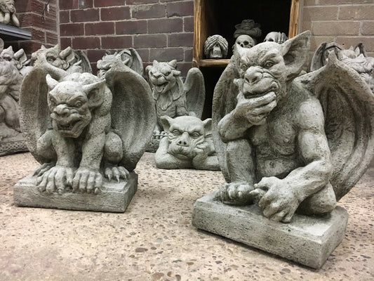 Pair of stone gargoyles with wings crouching on square bases, ideal for garden protection and gothic outdoor decor.