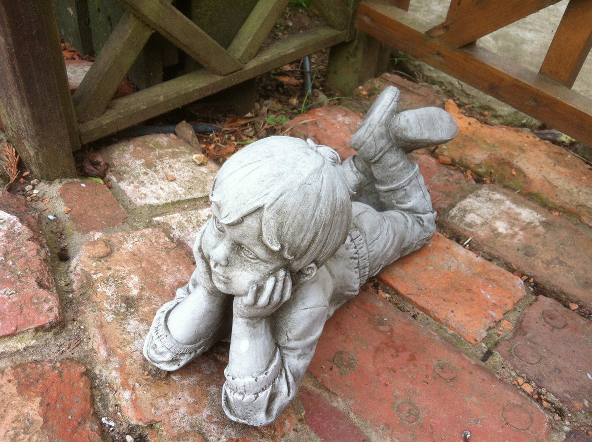Stone garden ornament boy laying on red brick path, detailed facial features and antique finish. Perfect for lawn or flowerbed decor.