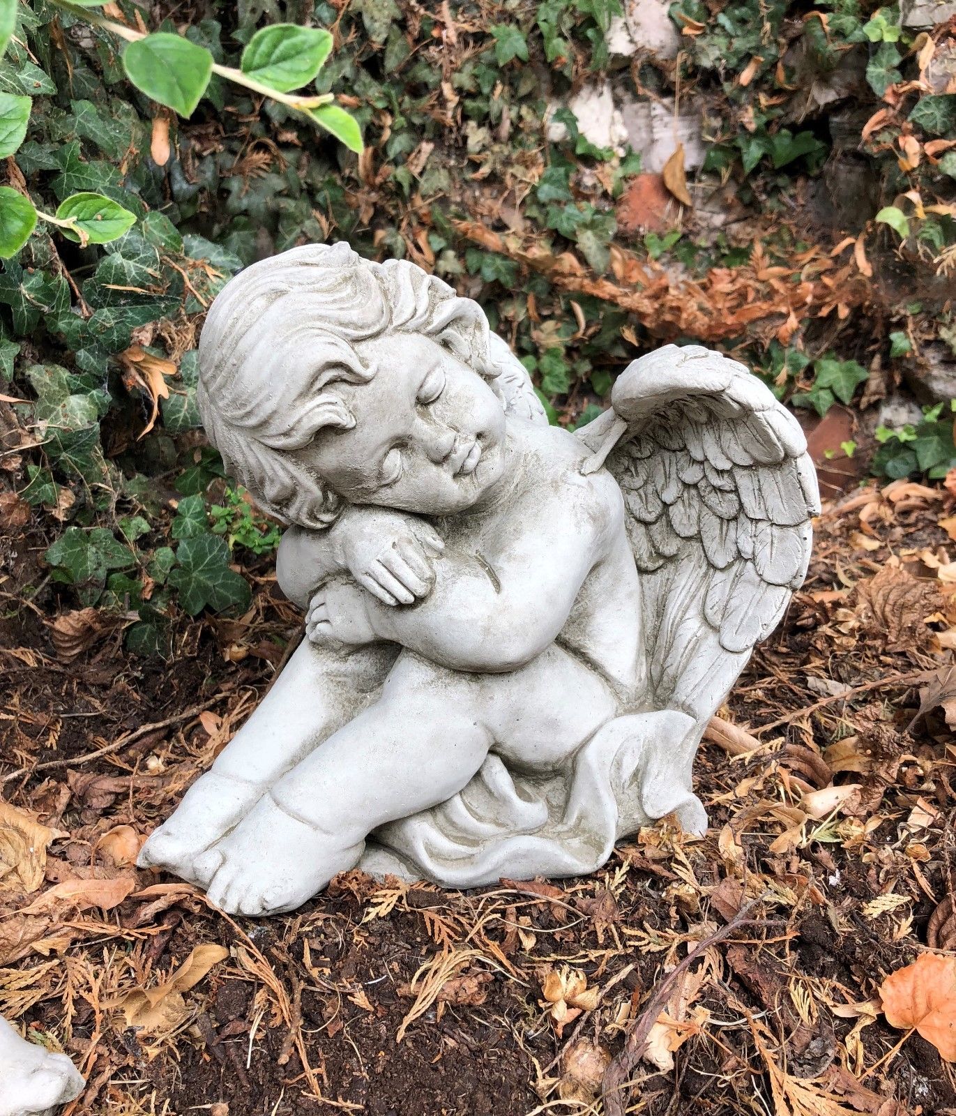 Close-up of sleeping stone winged baby angel sculpture. Detailed limestone ornament for serene garden or grave marker decor.