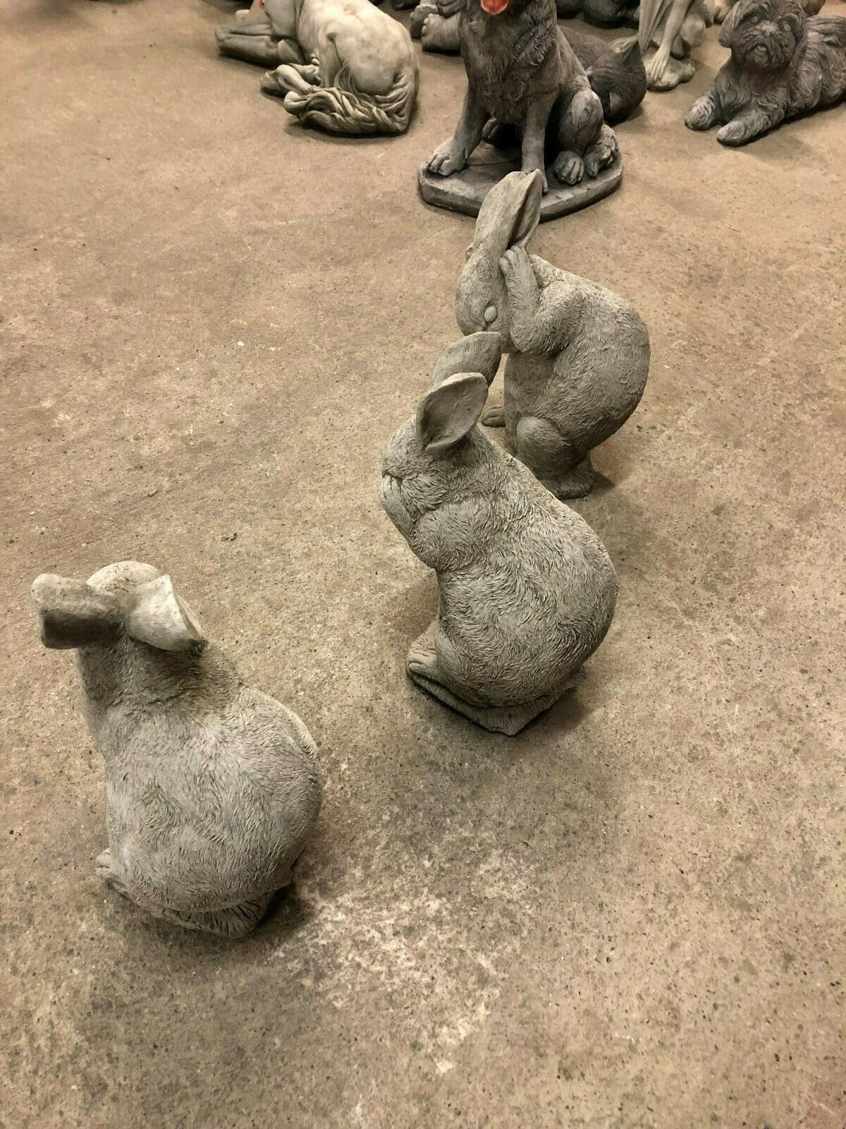 Top view of Rabbit Trio Statues in Hear, See, Speak No Evil poses, arranged in a row on concrete floor among other garden ornaments.