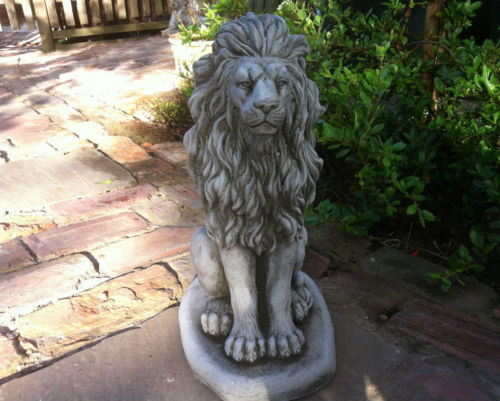 Front-facing stone lion statue on garden path, featuring intricate detailing and antique finish for elegant outdoor decoration.