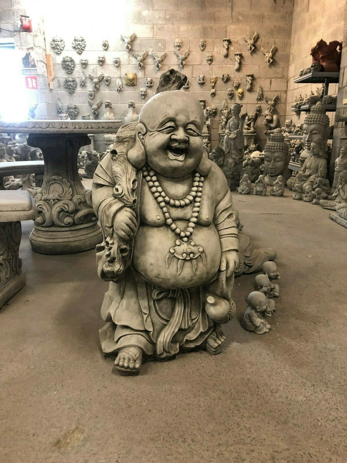 Durable stone Laughing Buddha Statue in indoor showroom, ideal for fortune-themed home or garden decoration. Features traditional sack and gourd.