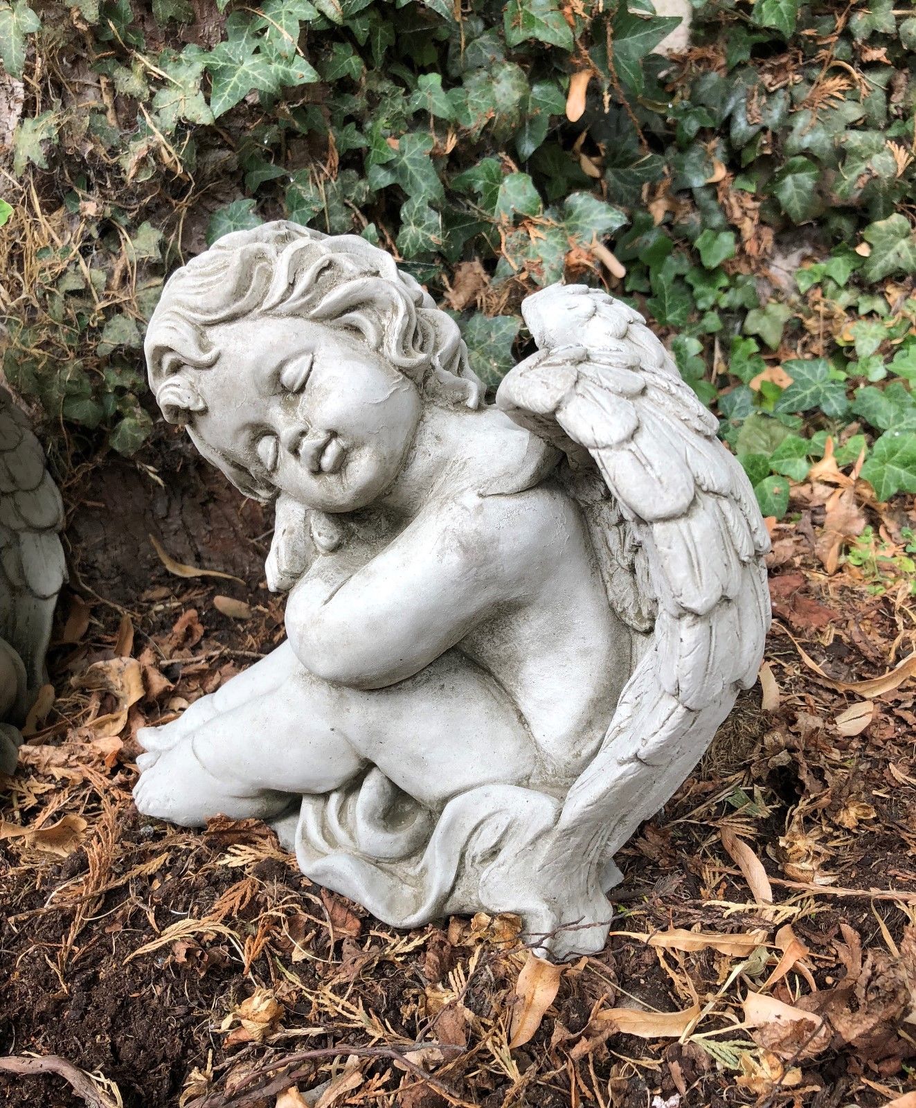 Detailed stone cherub angel with wings curled in sleep. Durable garden ornament for outdoor memorial or decorative landscaping.