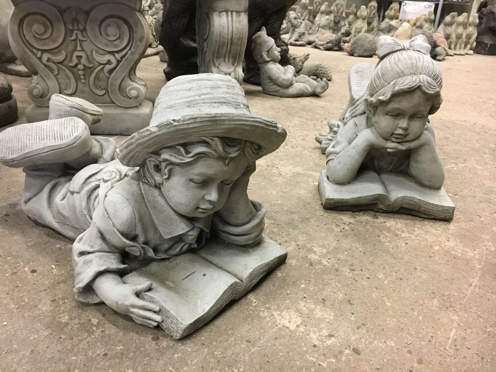 Reading Boy & Girl Statues in stone finish, lying down with books. Ideal garden decor with antique limestone detail and handmade charm.