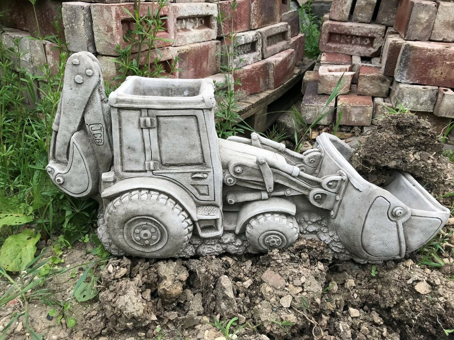 JCB Shovel Digger Planter - Garden Feature | Heavy & Durable limestone planter shaped like a digger, placed in soil near stacked bricks.