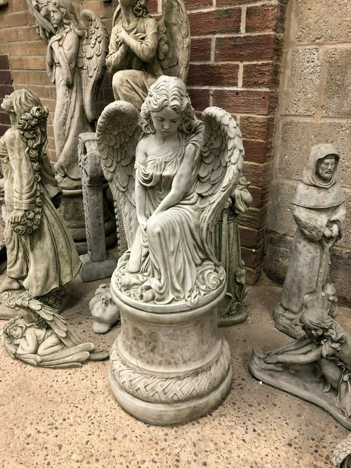Angel Garden Pedestal Statue - Stone Finish | Large & Durable. Kneeling angel sculpture with detailed wings on a round pedestal, ideal for outdoor decor.