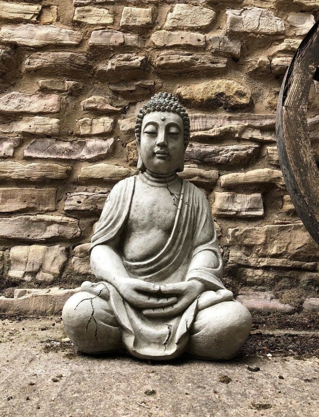 Stone Sitting Meditating Buddha Statue with antique finish, placed against rustic brick wall, ideal for garden serenity and outdoor decor.