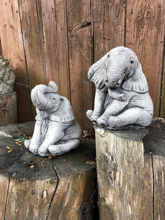 Pair of baby elephant ornaments in antique grey stone finish, displayed on tree stumps for garden decor. Ideal for outdoor lawn sculpture accents.