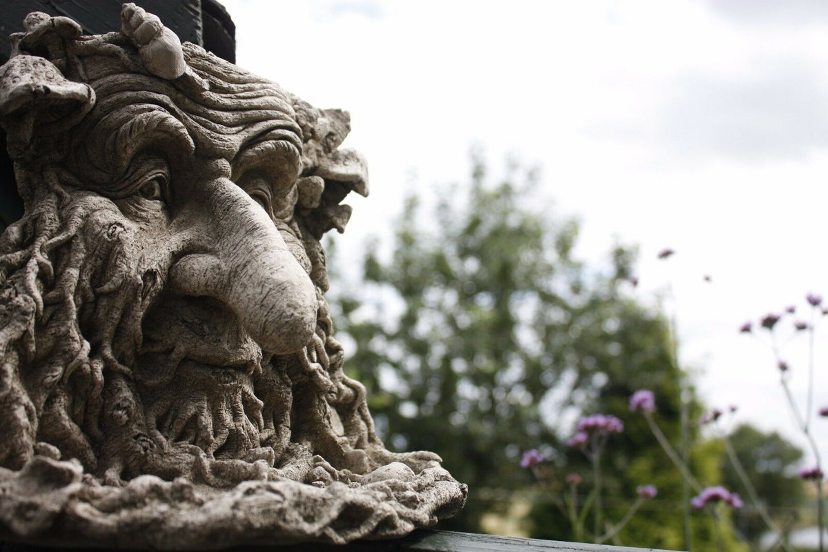 Greenman Bird Feeder Stone Ornament with long nose mounted on a garden post, showcasing detailed facial features and rustic antique finish.