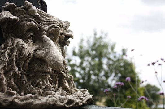 Greenman Bird Feeder Stone Ornament with long nose mounted on a garden post, showcasing detailed facial features and rustic antique finish.
